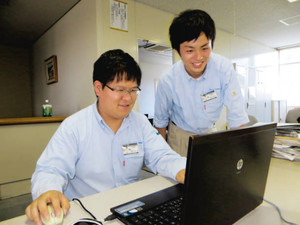 先輩社員の奥野宏平さんにデータ入力のアドバイスをもらう割貝壮一郎さん（左）＝千葉県松戸市の日立粉末冶金で