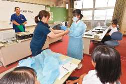 ウイルス感染を防ぐためのエプロンや手袋を試着する生徒＝いずれも鈴鹿市千代崎中で