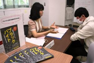 相談窓口で学生に対応する教員（左）。ブラックバイトへの注意喚起を呼びかけるチラシも置かれている＝愛知県春日井市の中部大で