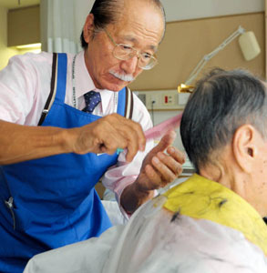 訪問先の病室で患者の髪をカットする藤田巌さん。「男前に仕上がりましたよ」＝東京都世田谷区の有隣病院で
